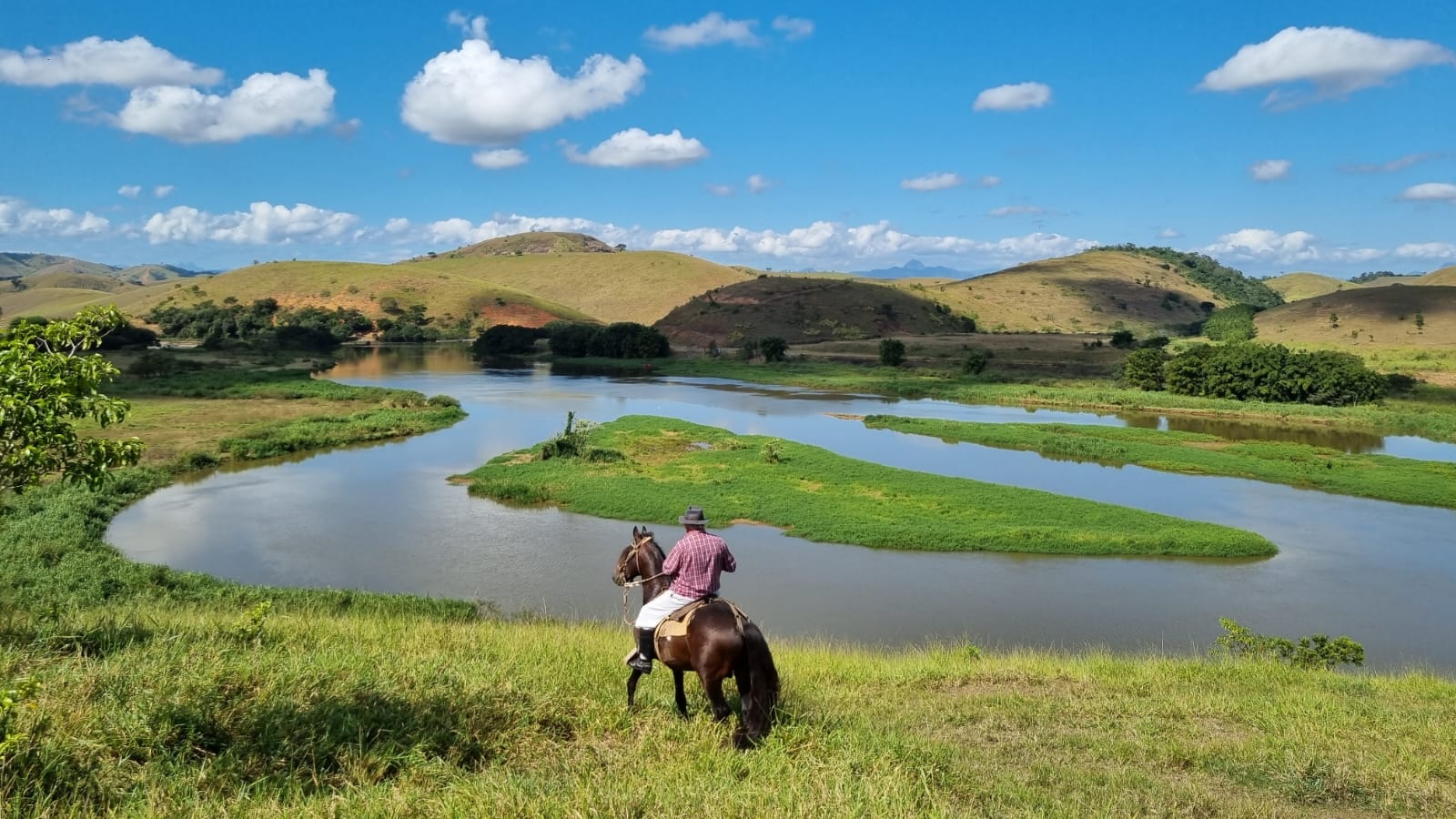 A person on horseback overlooking a river and rolling hills